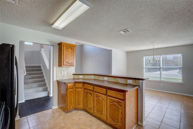 kitchen with light tile patterned floors, visible vents, freestanding refrigerator, a peninsula, and brown cabinetry