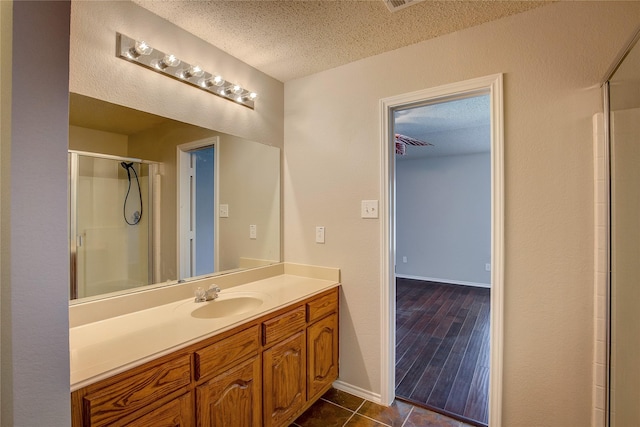 bathroom with vanity, baseboards, a textured ceiling, tile patterned floors, and a shower with shower door