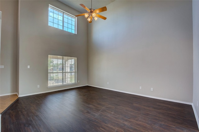 empty room with dark wood finished floors, baseboards, ceiling fan, and a towering ceiling