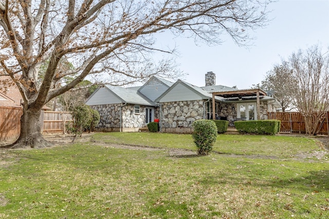 back of property with fence, a yard, stone siding, and a chimney