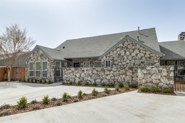 exterior space with stone siding, fence, and a shingled roof