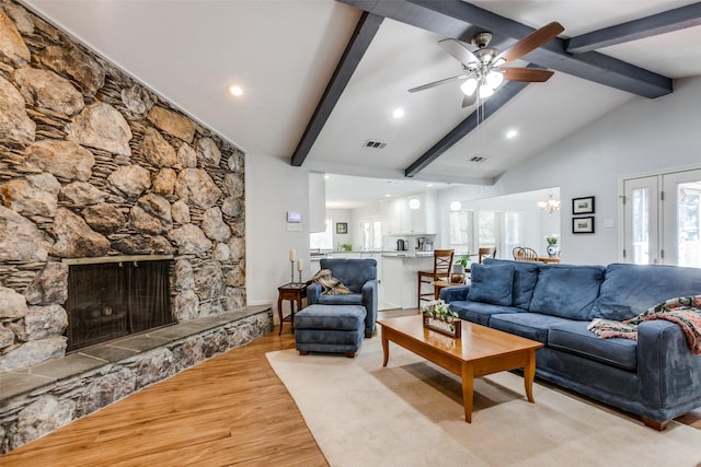 living room with visible vents, light wood-style floors, a fireplace, ceiling fan with notable chandelier, and vaulted ceiling with beams