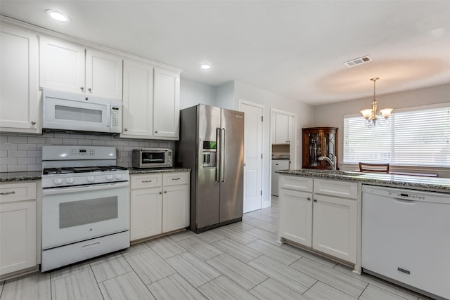 kitchen with white appliances, tasteful backsplash, white cabinets, visible vents, and a notable chandelier
