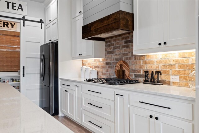 kitchen with tasteful backsplash, freestanding refrigerator, custom exhaust hood, white cabinetry, and gas cooktop