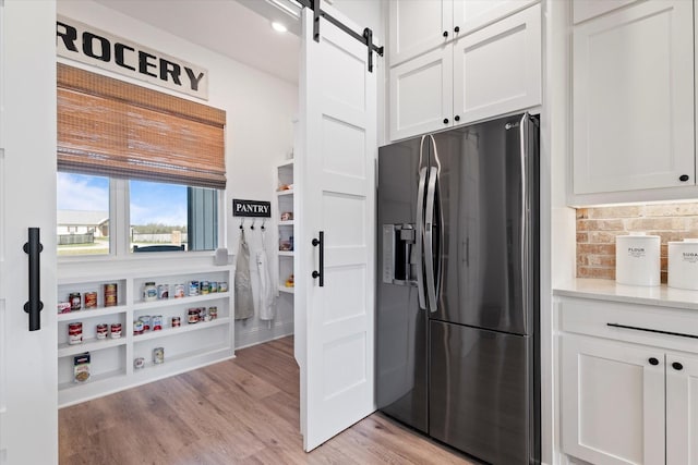 kitchen featuring a barn door, white cabinets, stainless steel refrigerator with ice dispenser, and light wood finished floors