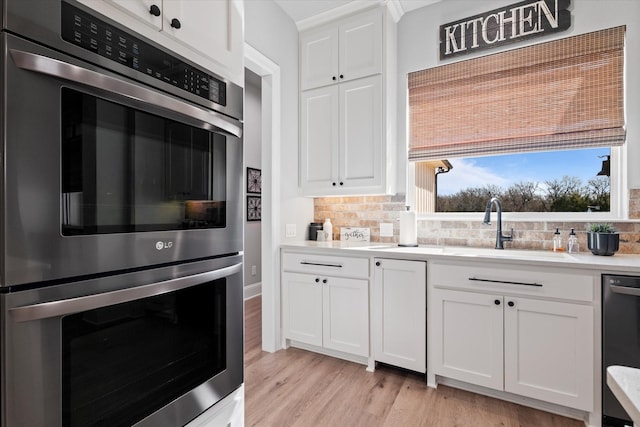 kitchen with light wood-style flooring, tasteful backsplash, stainless steel double oven, light countertops, and dishwashing machine