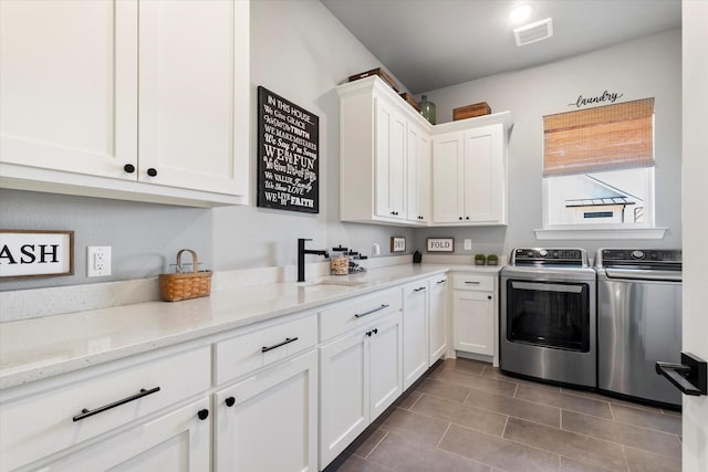 clothes washing area with visible vents, dark tile patterned floors, a sink, cabinet space, and washing machine and clothes dryer