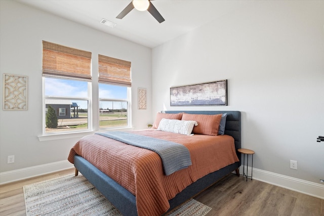 bedroom with ceiling fan, wood finished floors, visible vents, and baseboards