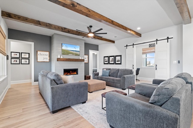 living area featuring light wood finished floors, a large fireplace, ceiling fan, baseboards, and a barn door