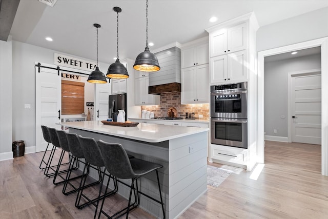 kitchen with tasteful backsplash, light wood finished floors, freestanding refrigerator, stainless steel double oven, and gas stovetop