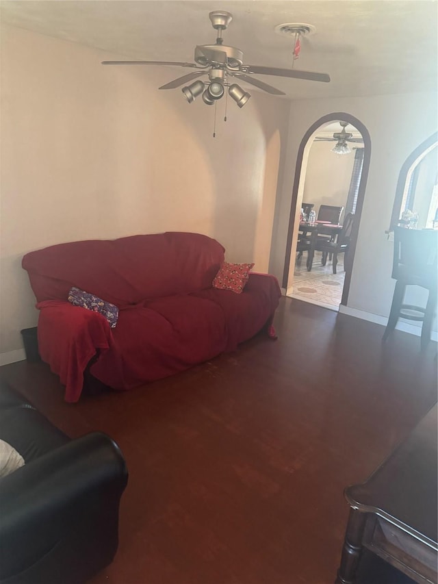 living room with arched walkways, visible vents, baseboards, and ceiling fan