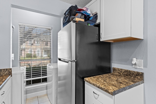 kitchen with washer / dryer, white cabinets, light tile patterned floors, and freestanding refrigerator
