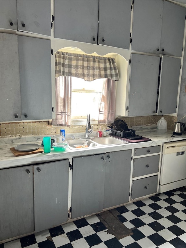 kitchen with light floors, light countertops, decorative backsplash, white dishwasher, and a sink