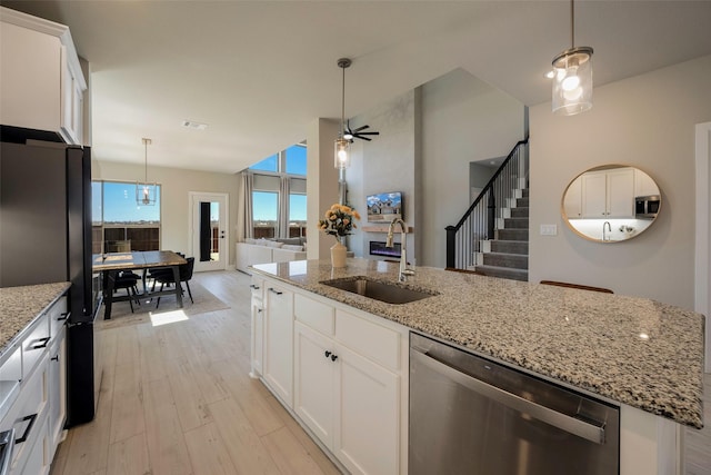 kitchen with a sink, open floor plan, white cabinetry, light wood-style floors, and appliances with stainless steel finishes