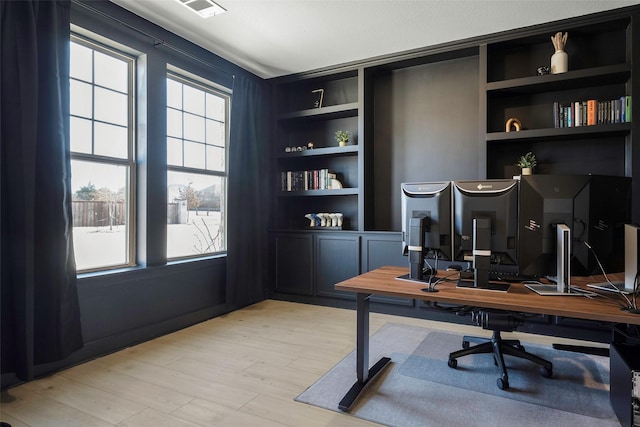 office area featuring light wood-style flooring, visible vents, a wealth of natural light, and built in shelves