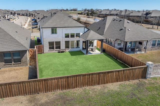 rear view of property featuring a shingled roof, a fenced backyard, a patio, brick siding, and a residential view