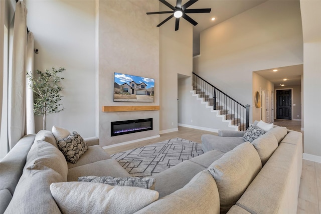 living room featuring a glass covered fireplace, light wood-style floors, a high ceiling, ceiling fan, and baseboards
