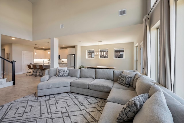 living area featuring stairway, a high ceiling, visible vents, baseboards, and light wood-style flooring