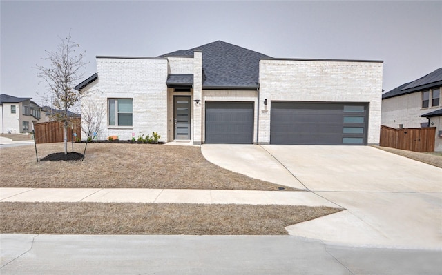 modern home with brick siding, an attached garage, concrete driveway, and fence