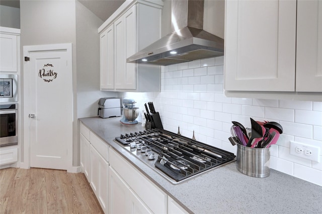 kitchen with wall chimney range hood, light wood-style floors, white cabinets, and stainless steel appliances