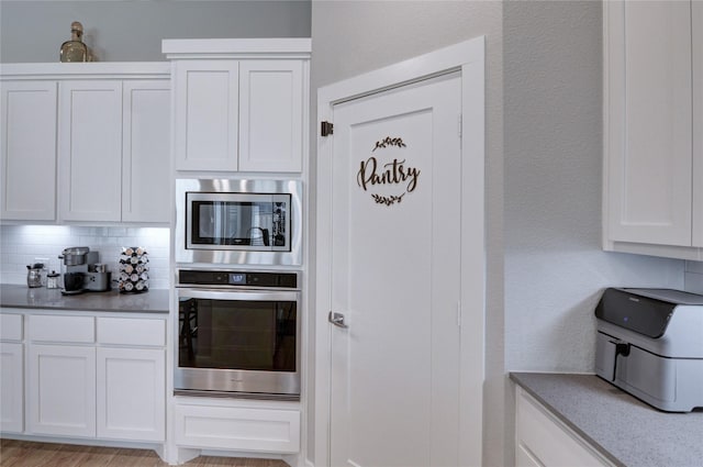 kitchen with decorative backsplash, white cabinets, a textured wall, and appliances with stainless steel finishes