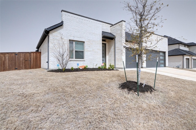 view of front of home featuring driveway, brick siding, an attached garage, and fence