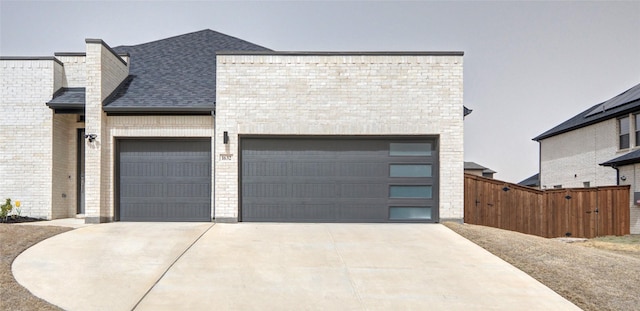 view of front of property featuring fence, roof with shingles, an attached garage, concrete driveway, and brick siding