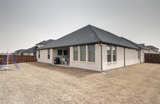 rear view of property featuring brick siding, a playground, roof with shingles, a fenced backyard, and a patio