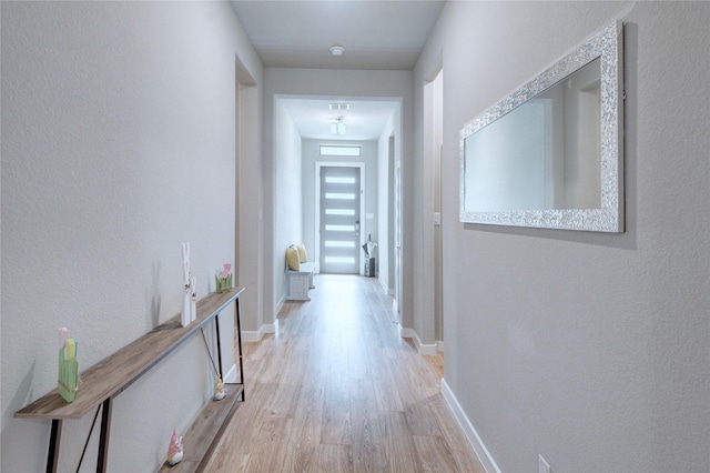 hall featuring light wood-style flooring, visible vents, and baseboards