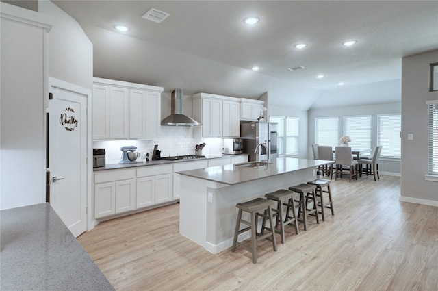 kitchen featuring a sink, wall chimney range hood, a breakfast bar, appliances with stainless steel finishes, and a kitchen island with sink