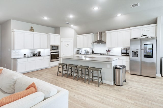 kitchen with light wood-type flooring, visible vents, a breakfast bar, appliances with stainless steel finishes, and wall chimney exhaust hood