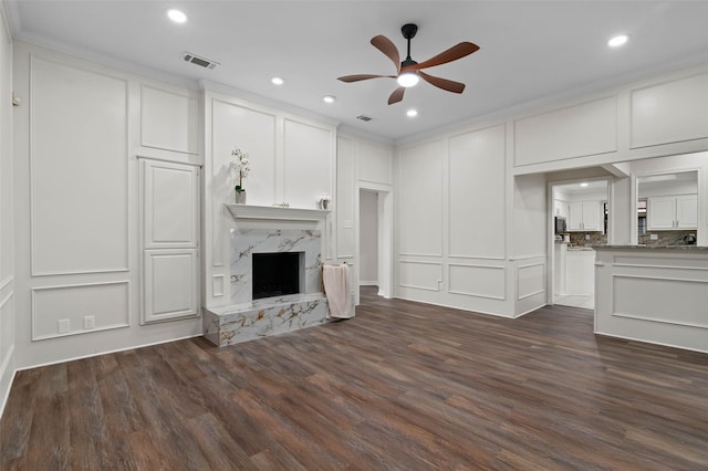 unfurnished living room featuring visible vents, a high end fireplace, dark wood-style flooring, a decorative wall, and a ceiling fan