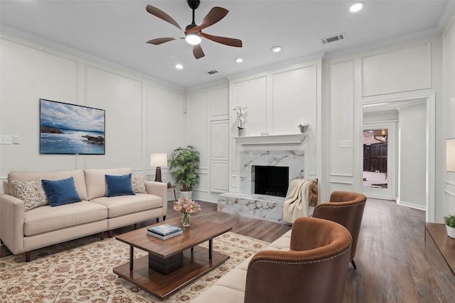 living room with ceiling fan, visible vents, a decorative wall, ornamental molding, and wood finished floors