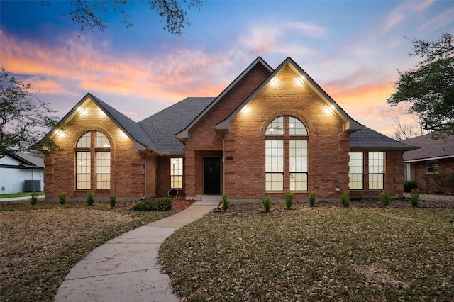 view of front of property featuring central air condition unit, a shingled roof, french doors, and brick siding