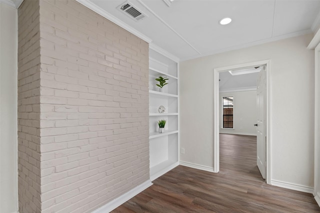 corridor featuring brick wall, ornamental molding, dark wood-style flooring, baseboards, and visible vents
