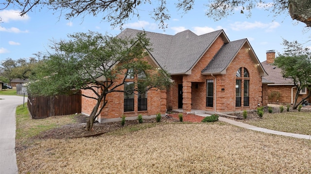 view of front of property featuring fence, roof with shingles, and brick siding