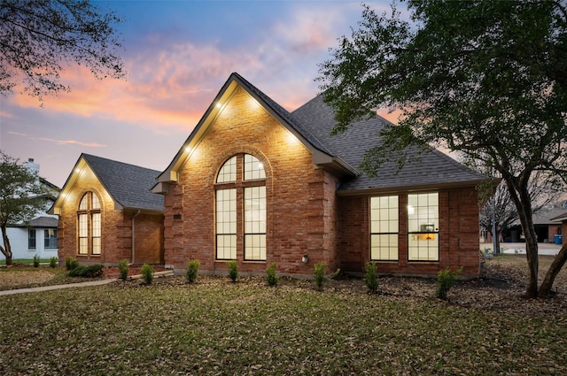view of front of home with brick siding, french doors, a shingled roof, and a lawn