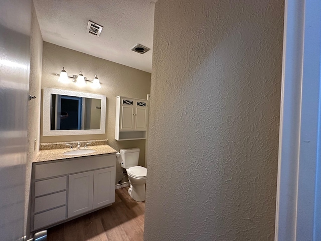 2612 Lemmontree Ln, Plano, TX 75074 - half bathroom featuring a textured wall, toilet, wood finished floors, vanity, and a textured ceiling