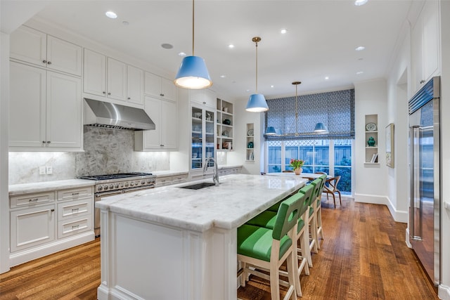 kitchen featuring under cabinet range hood, wood finished floors, white cabinetry, high end appliances, and a sink