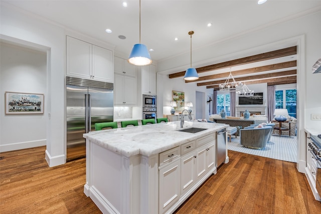 kitchen with a center island with sink, a sink, wood finished floors, white cabinets, and built in appliances