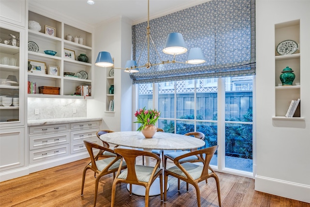 dining area with baseboards, light wood-style floors, built in shelves, and crown molding