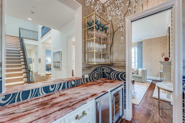 bar featuring stairway, wood finished floors, wallpapered walls, a bar, and crown molding