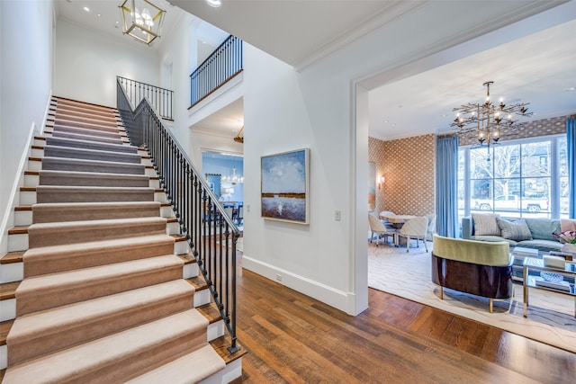 stairs with a chandelier, crown molding, and wallpapered walls