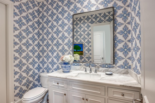 bathroom featuring toilet, wallpapered walls, and vanity
