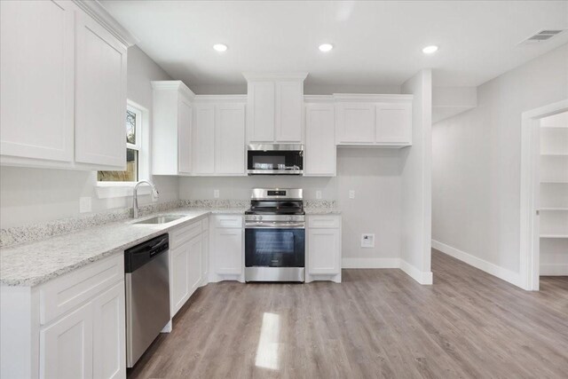 kitchen featuring baseboards, light wood-style flooring, a sink, stainless steel appliances, and white cabinets