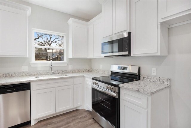 kitchen with a sink, stainless steel appliances, light wood-style floors, and white cabinetry