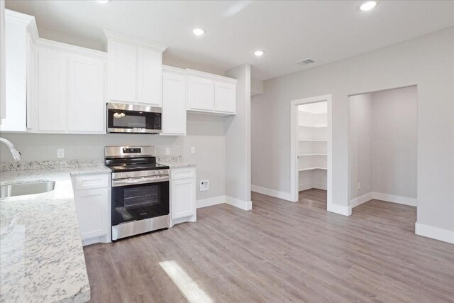 kitchen with visible vents, a sink, light stone counters, appliances with stainless steel finishes, and white cabinets