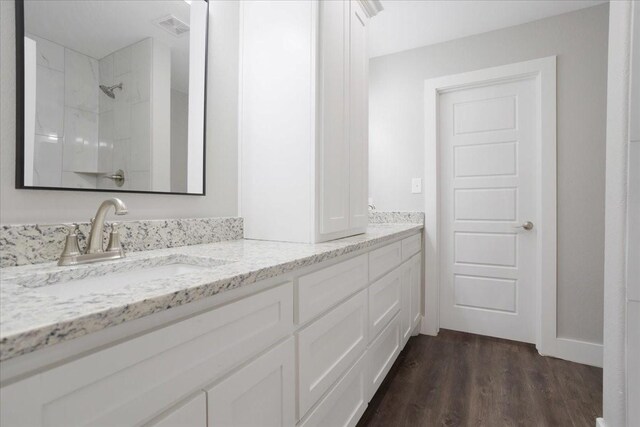 full bath featuring wood finished floors, visible vents, double vanity, a sink, and a shower