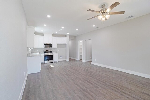 unfurnished living room with visible vents, light wood-style flooring, a sink, baseboards, and ceiling fan