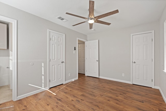 unfurnished bedroom with visible vents, ensuite bath, wood finished floors, baseboards, and ceiling fan